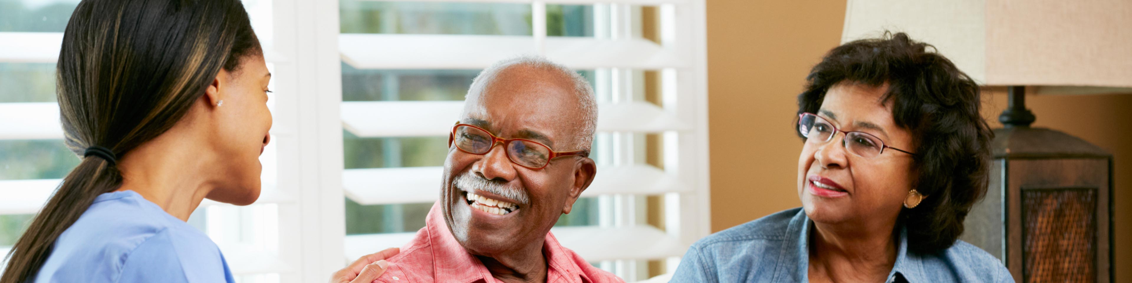 a woman taking notes and speaking with an older couple sitting on a couch