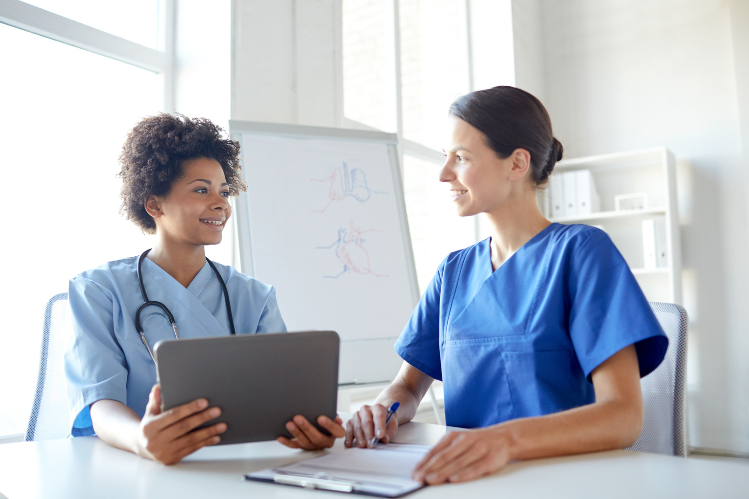 Two nurses sit at table using nursing simulation software on tablet