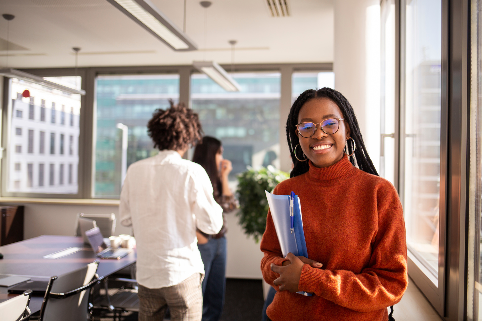 Young woman in office in foreground is looking at camera