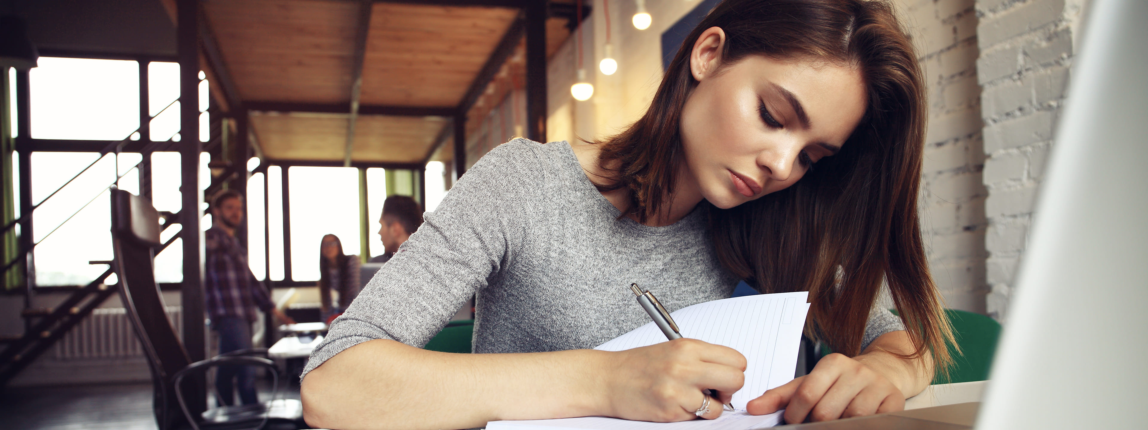 vrouw schrijft iets op papier en zit achter laptop