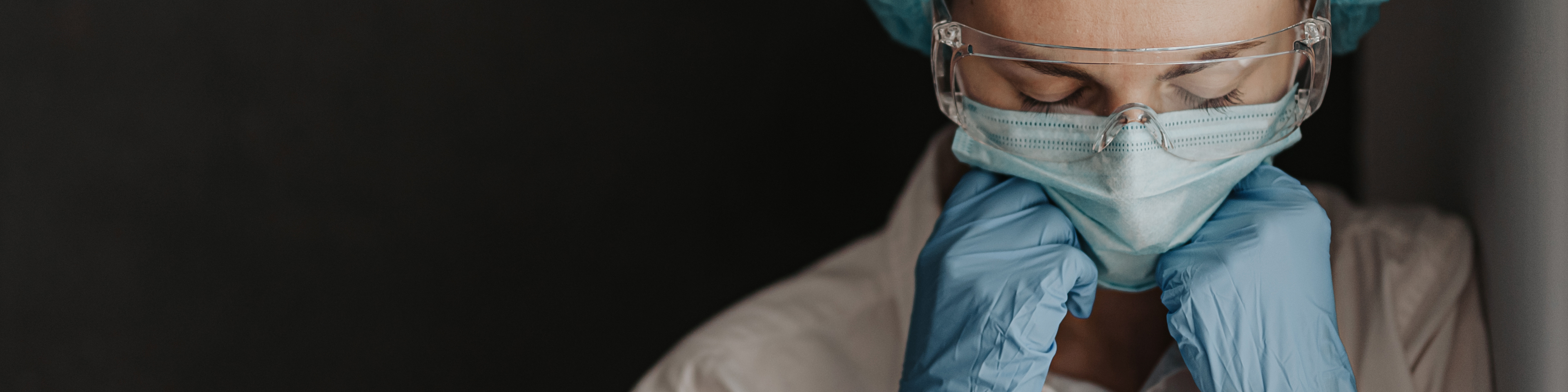 Tired medical worker, wearing protective medical gear, leaning chin into their hands