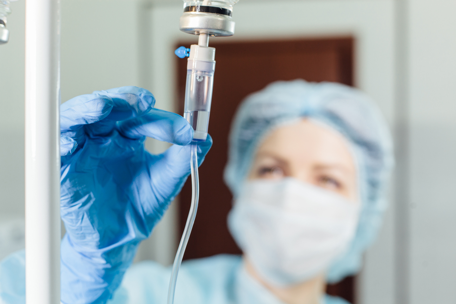 Masked nurse connecting an intravenous drip in hospital room