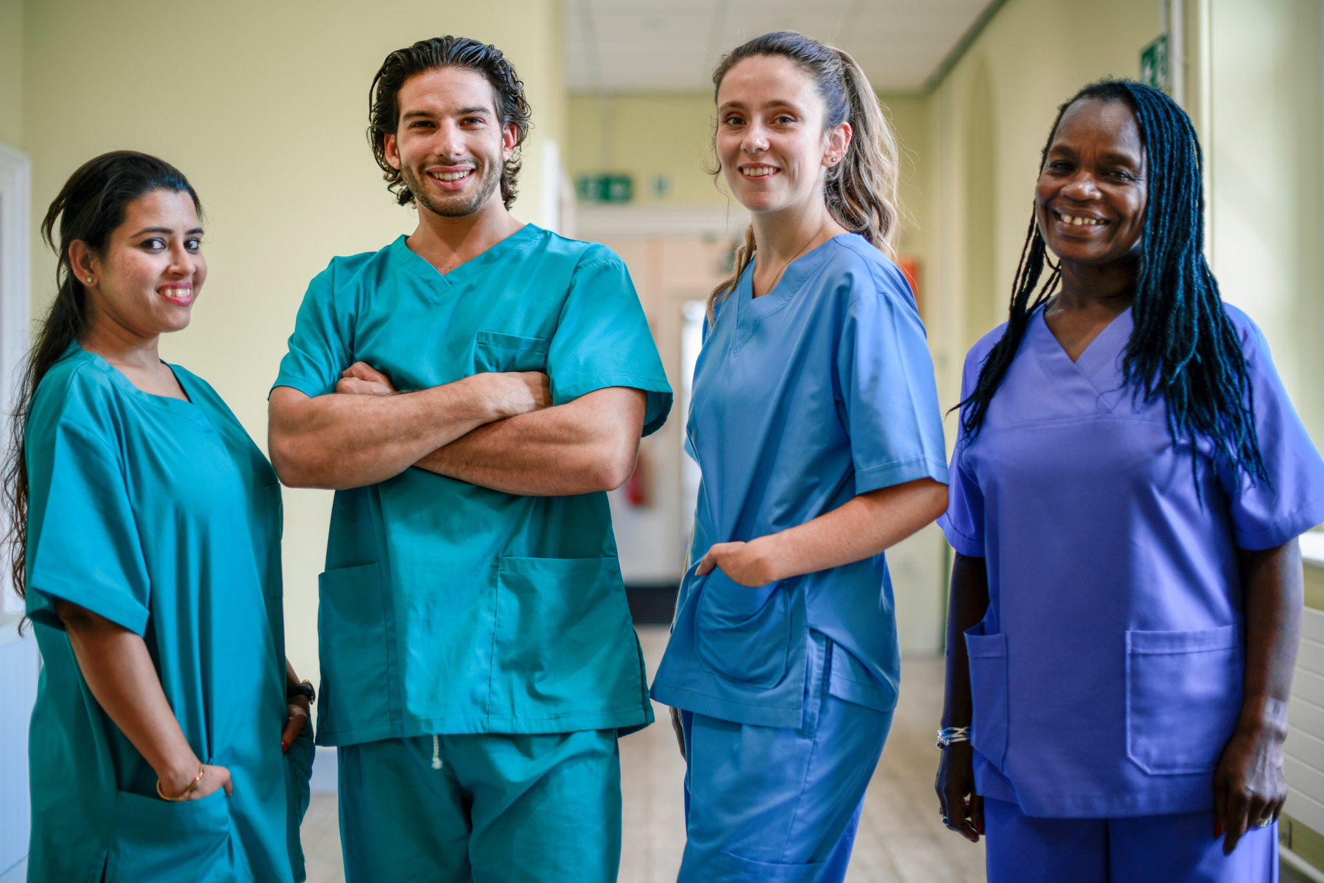 Nursing team wearing blue scrubs, standing in a row of four, smiling at the camera