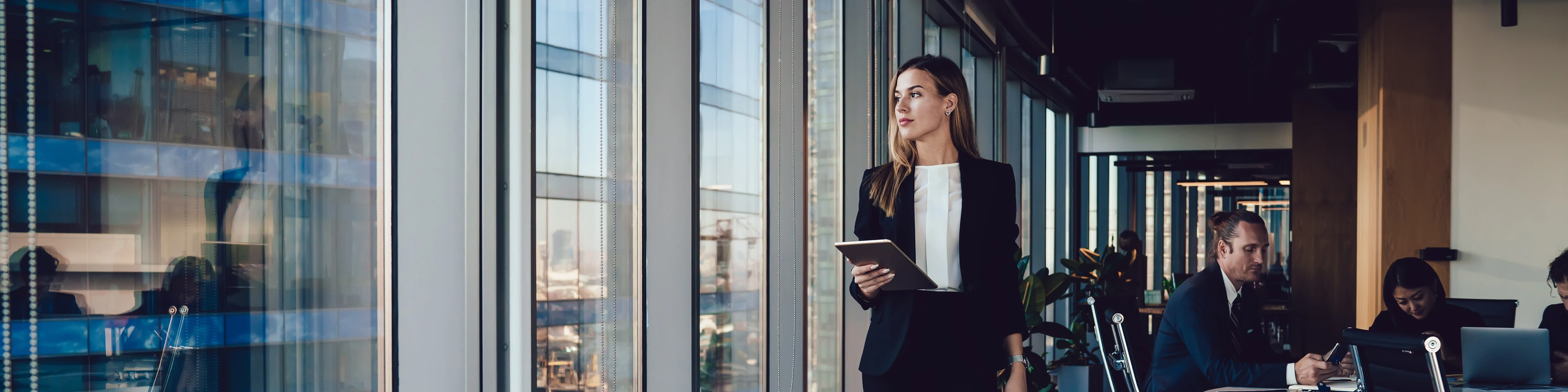 Serious female administrative manager in formal suit walking in office with digital tablet for checking office working process