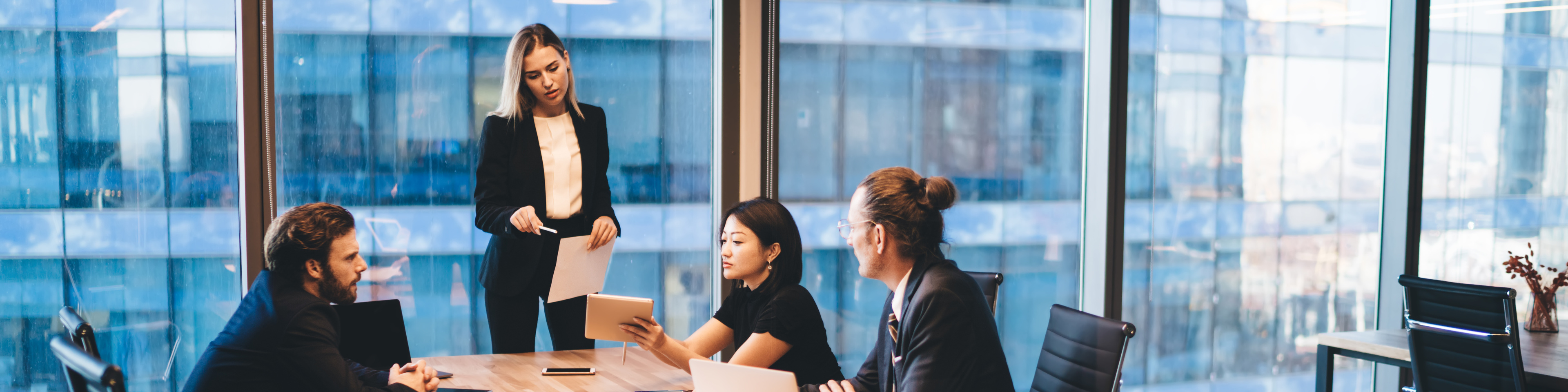 Business meeting with 4 people sitting around a conference table with a glass wall behind them