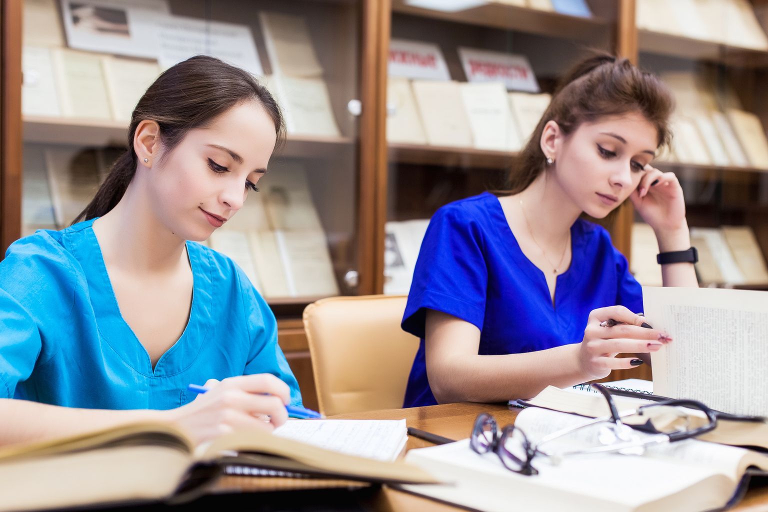 Two medical students searching through textbooks in nursing school