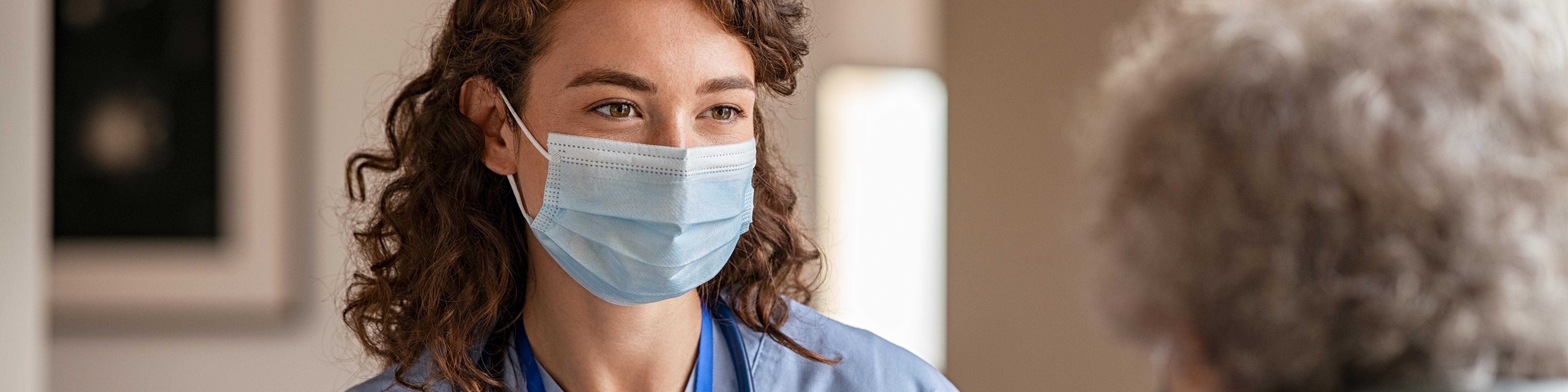 Young doctor visits senior woman with surgical mask.