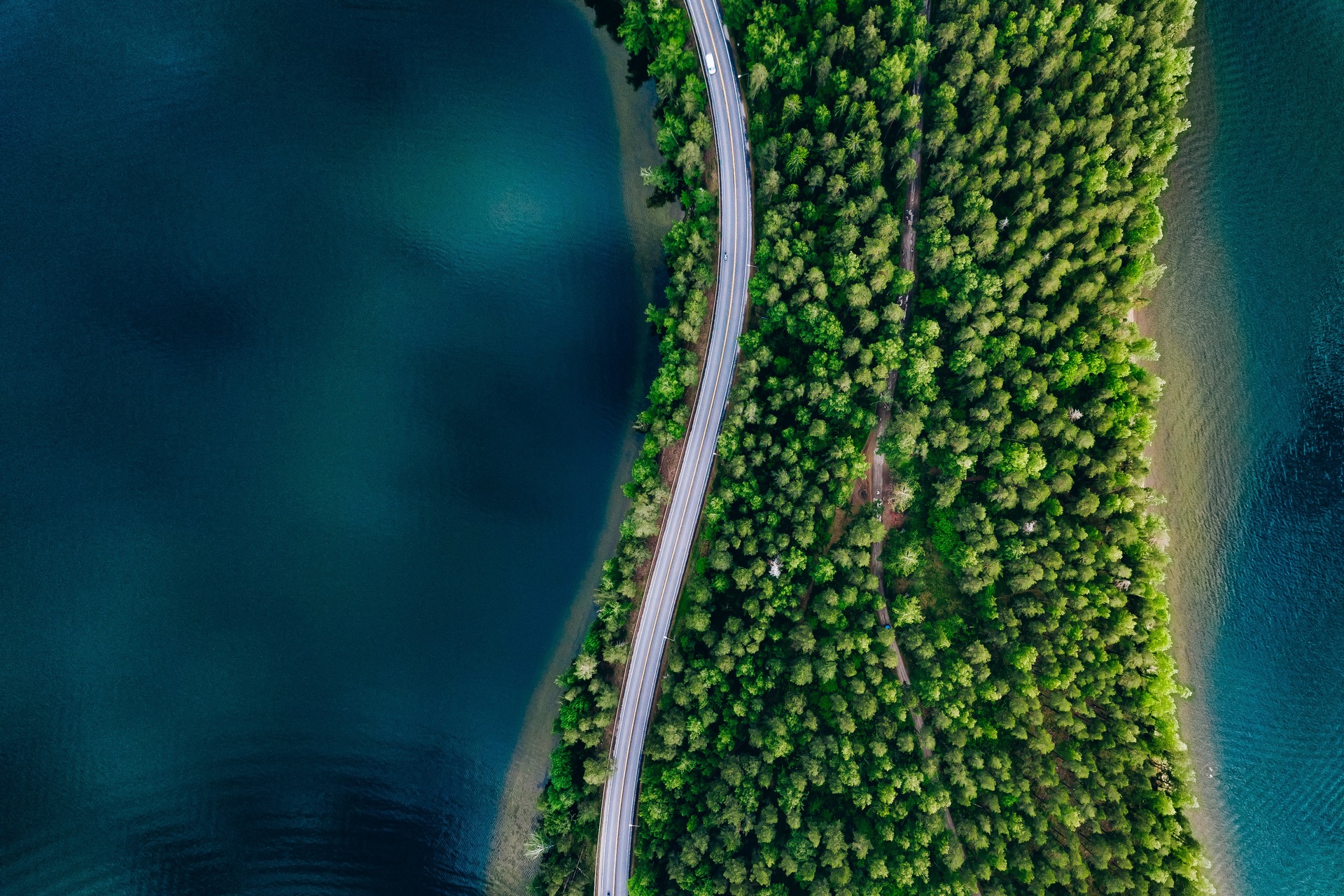Aerial view of road between green forest and blue lake in Finland, 
