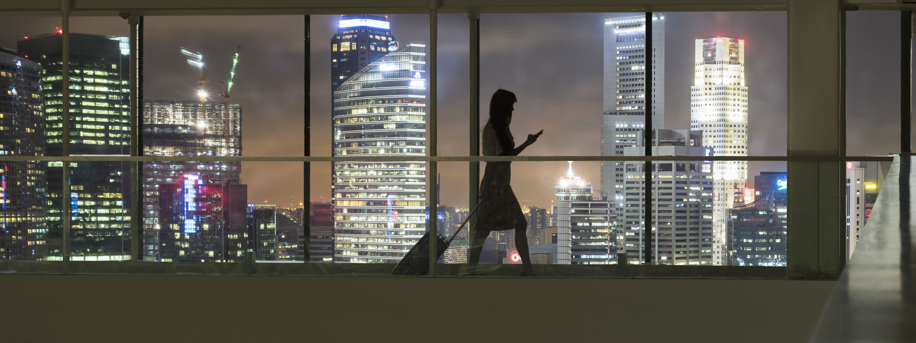 Young woman using smartphone and pulling suitcase, city skyline in view 