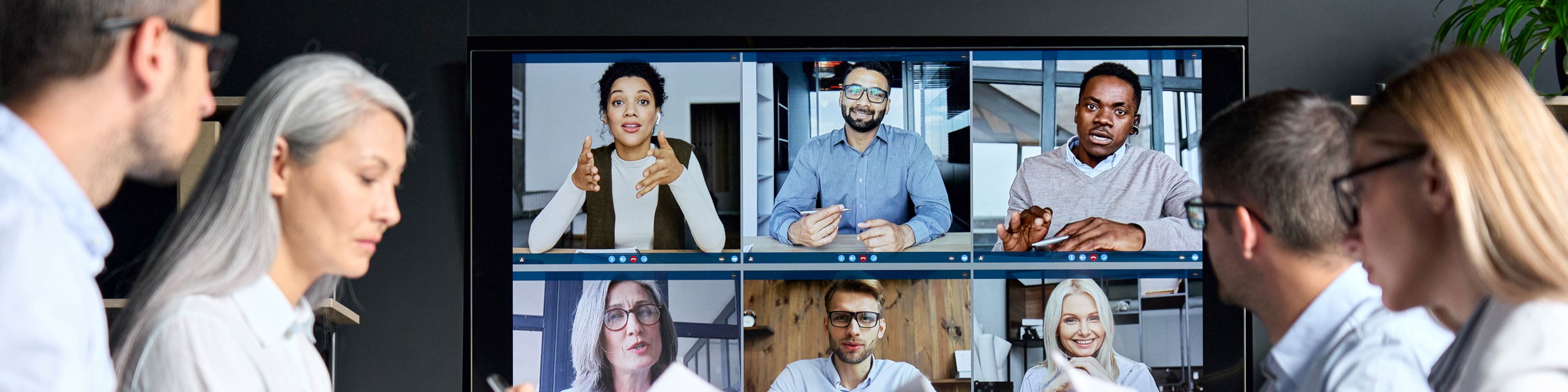 Four businesspeople conducting a meeting with others attending via Zoom