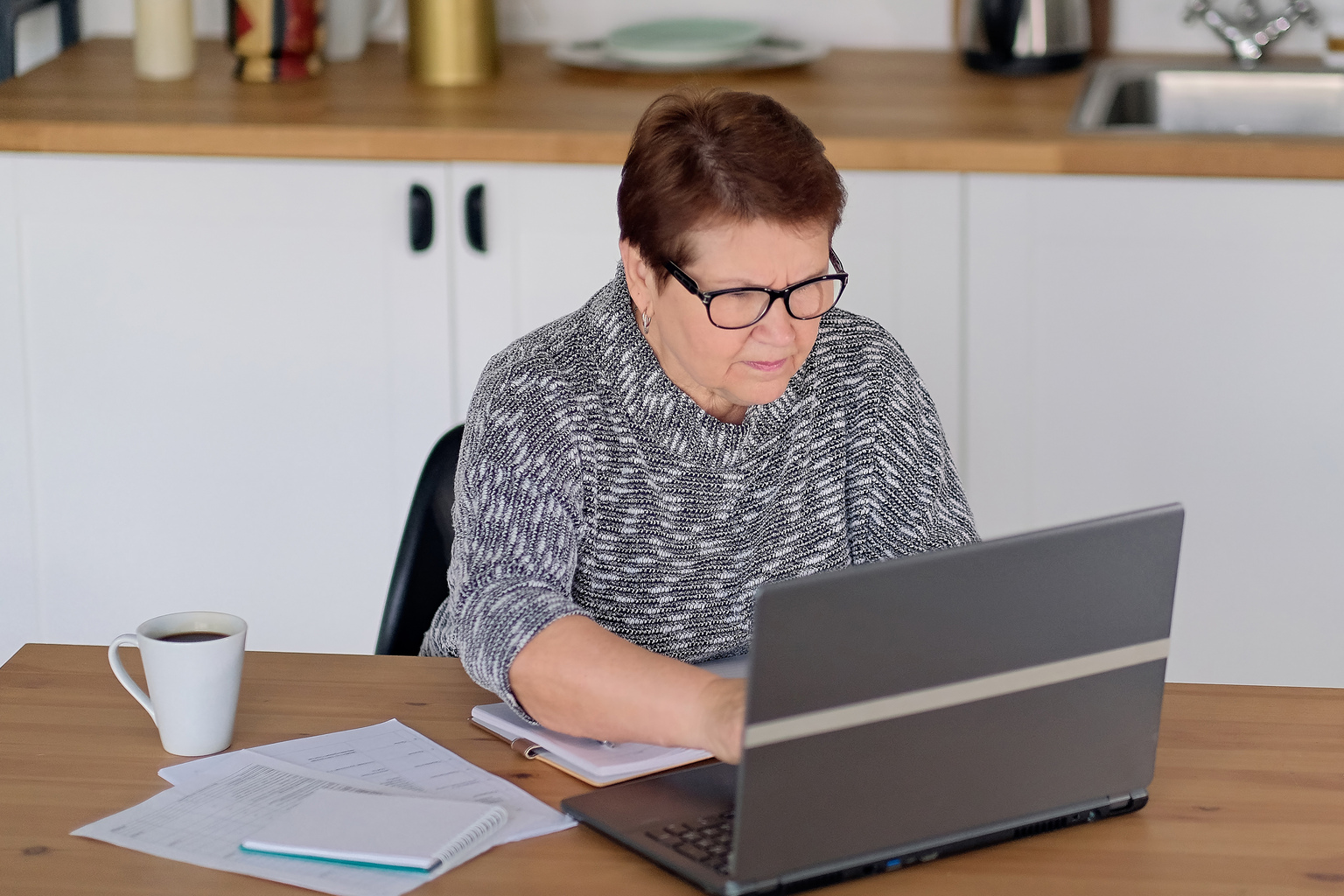 Senior woman using laptop for websurfing in her kitchen