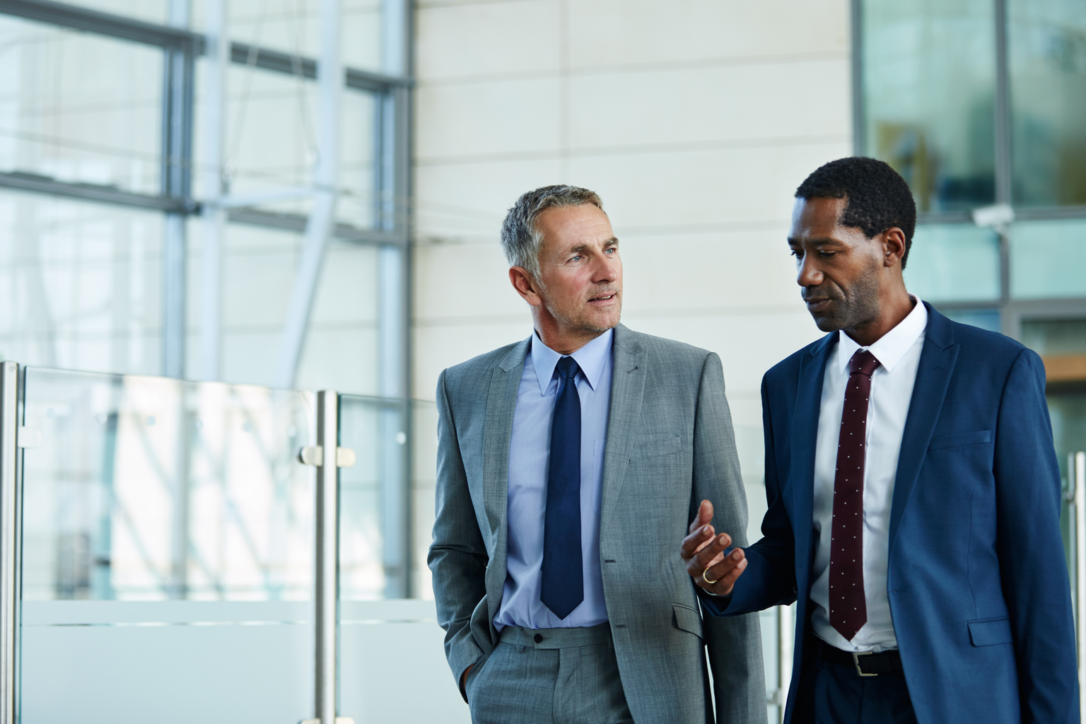 Shot of two businessmen walking and talking together in the lobby of an office building