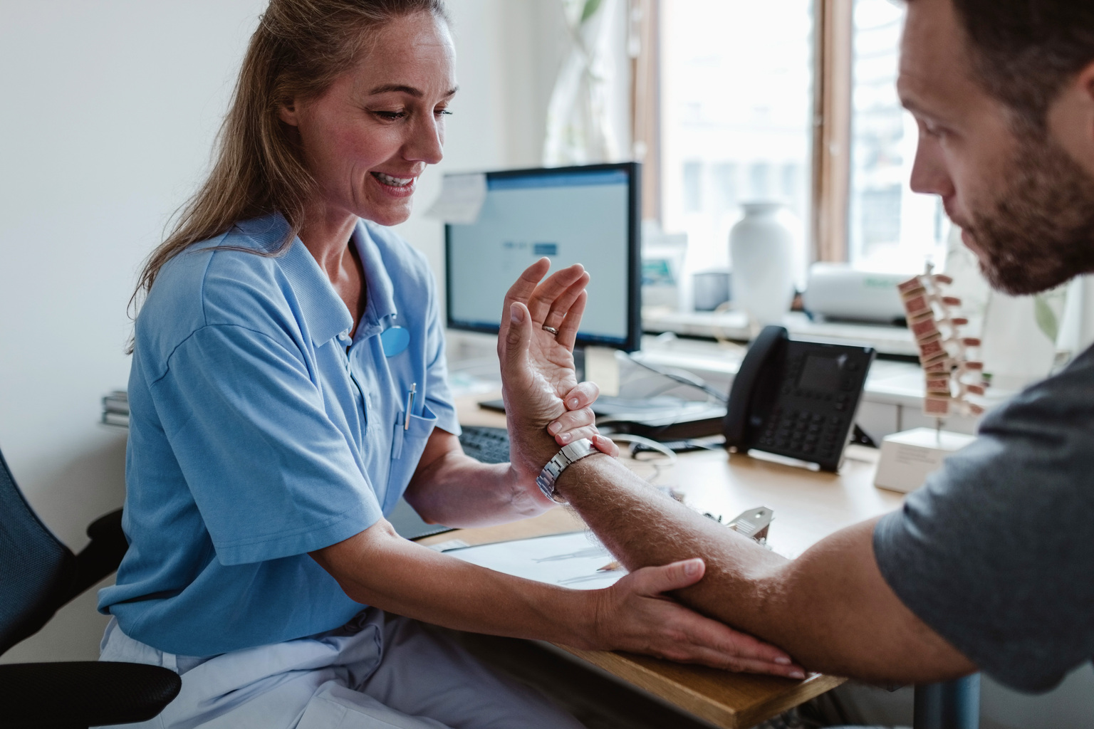 White female doctor examining male patient's hand.