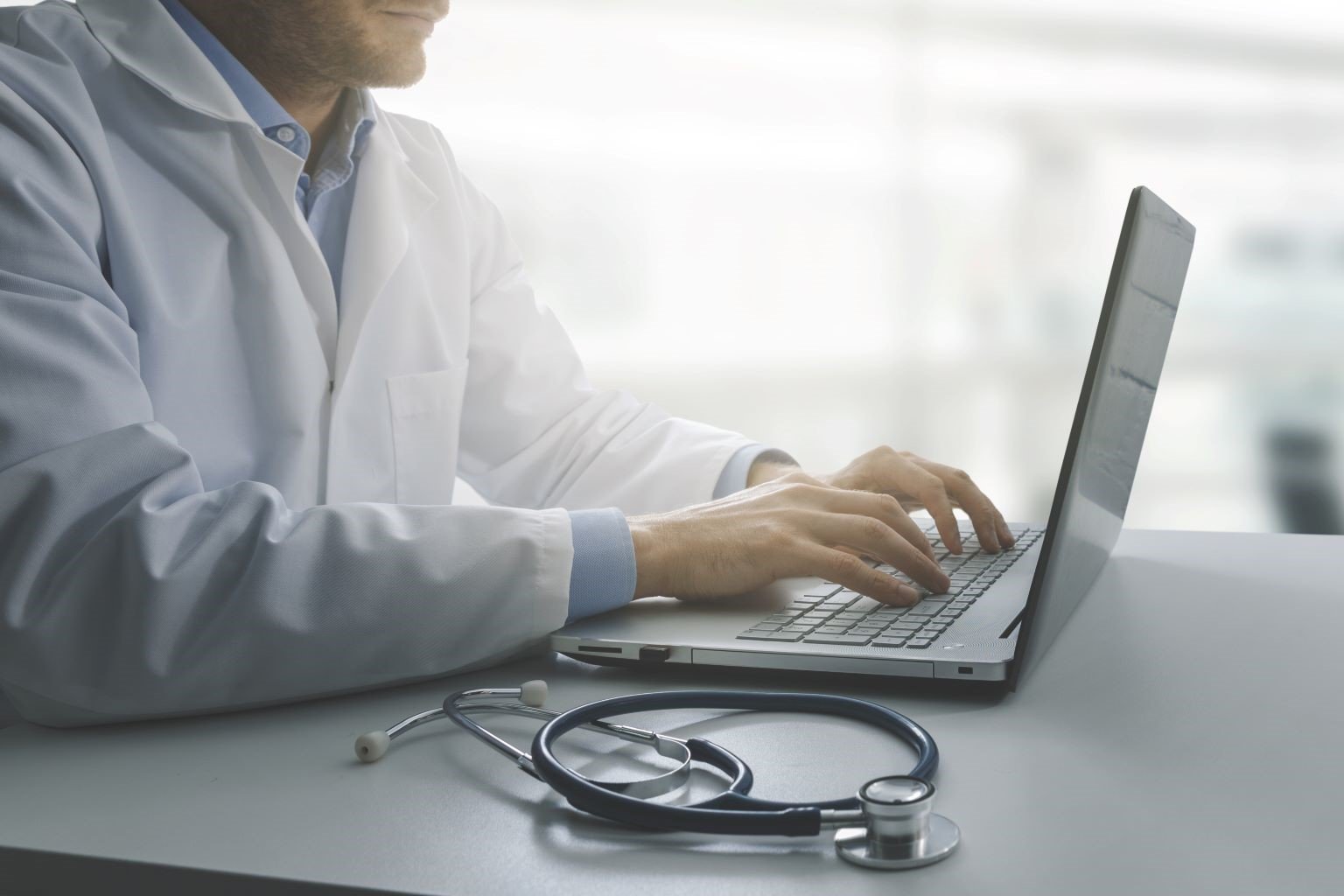 Male doctor typing on laptop at desk.