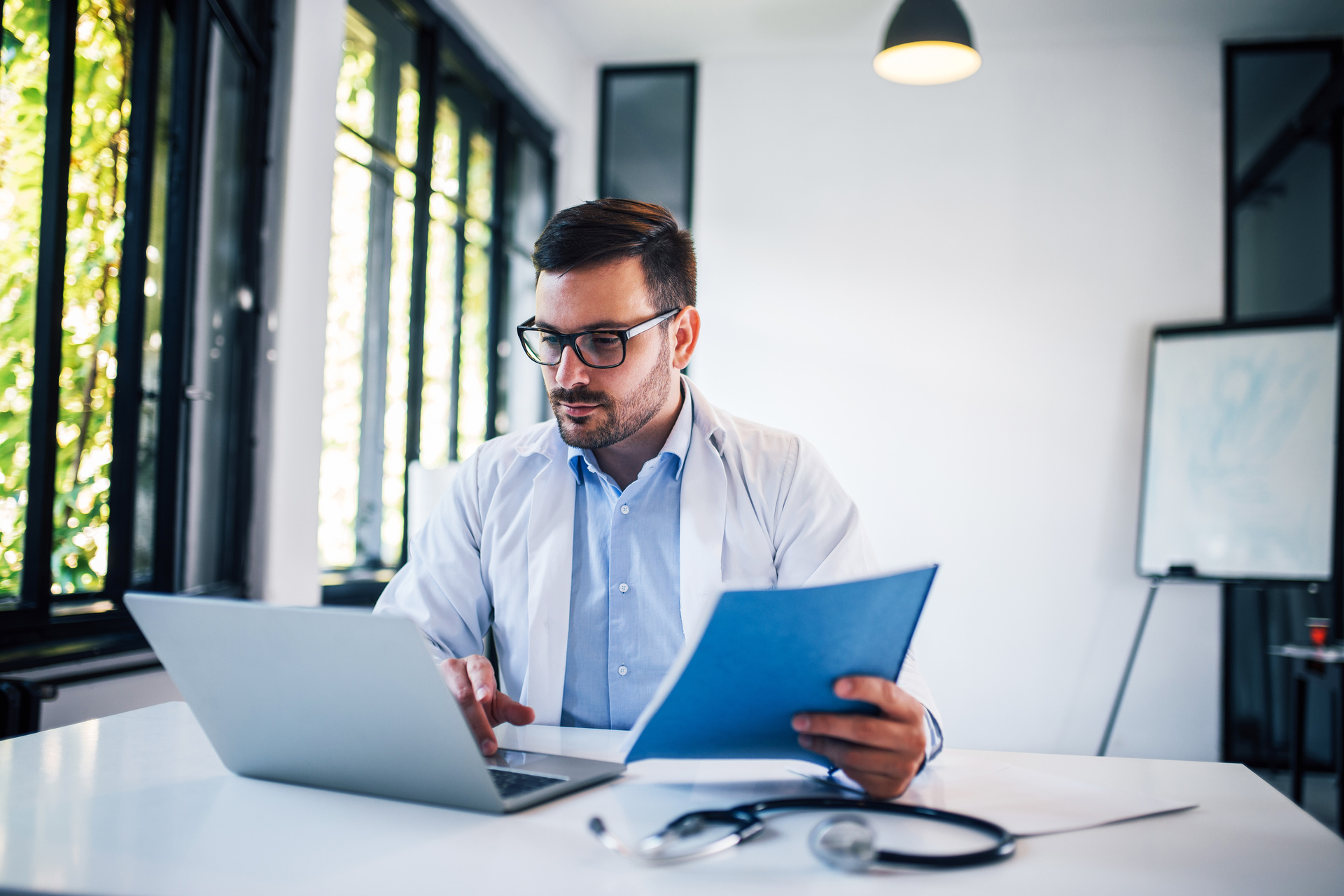 Male doctor working at laptop, seated at table