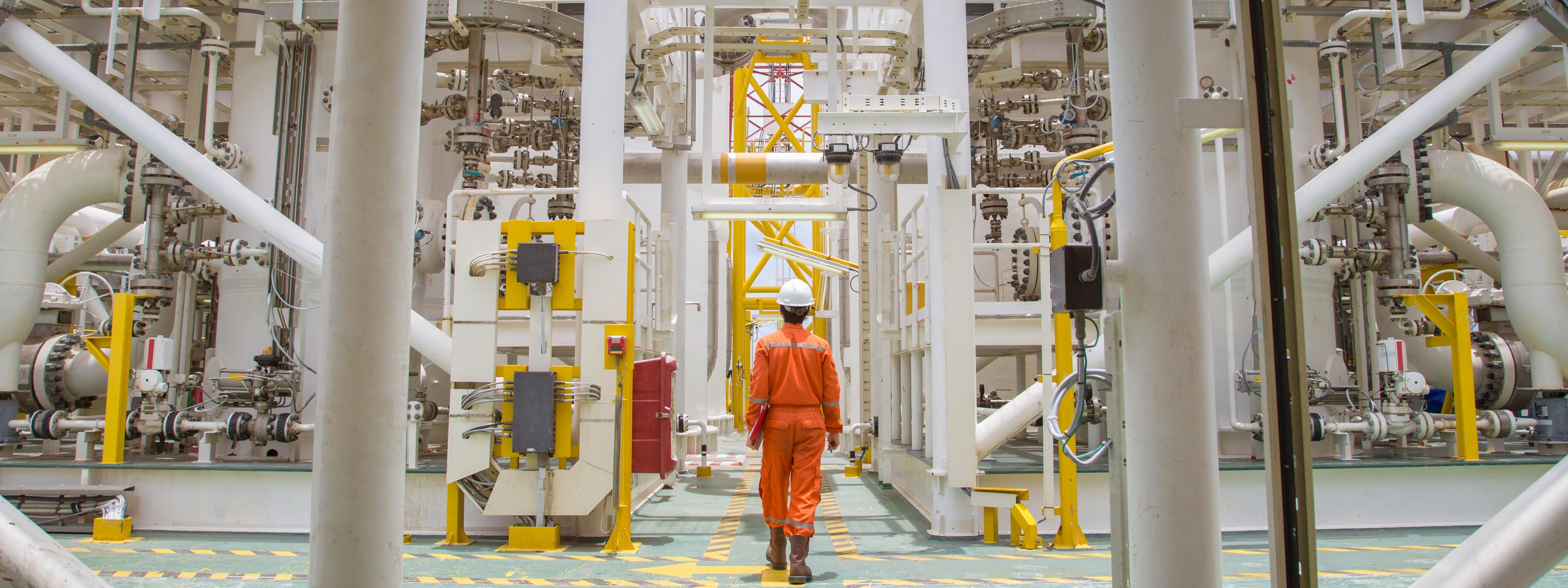 Technician walking through offshore oil and gas process for checking the condition of equipment on platform.