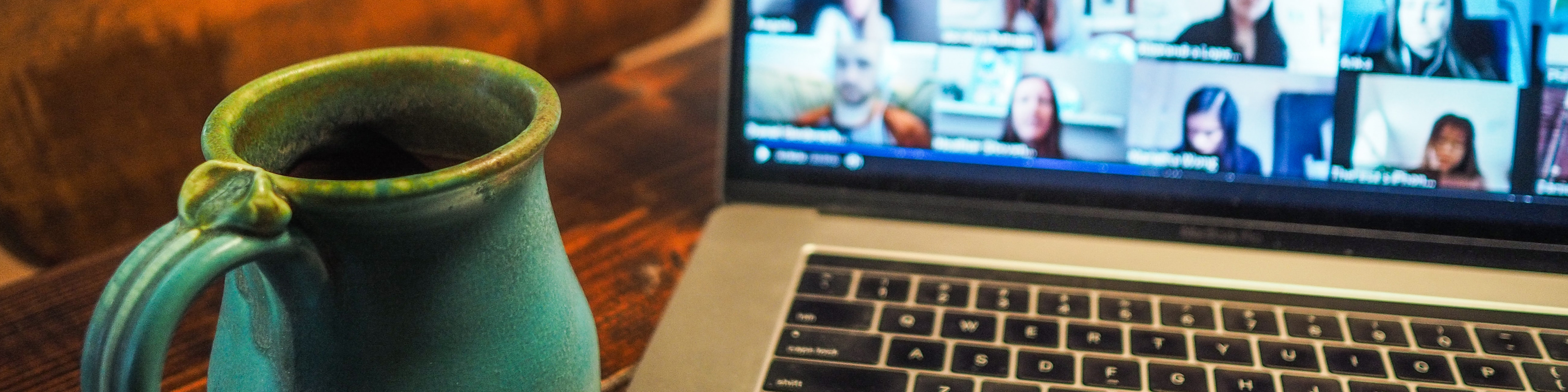 Zoom call on a laptop with coffee mug next to it on table