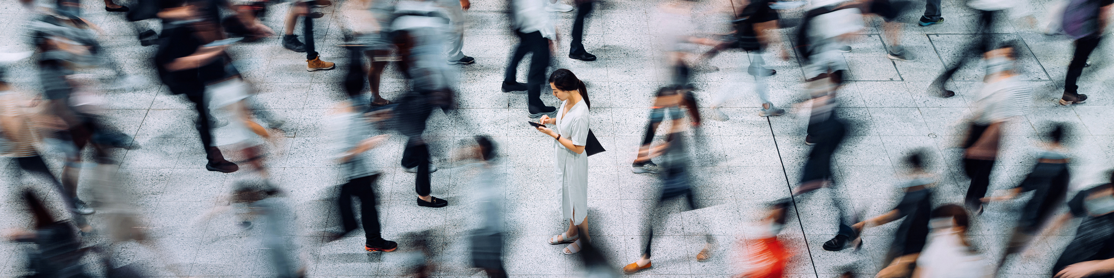 Focus shot with Asian woman with grey dress standing in a crowd looking at her phone, Q3 2021, TAA NA US - Preparer