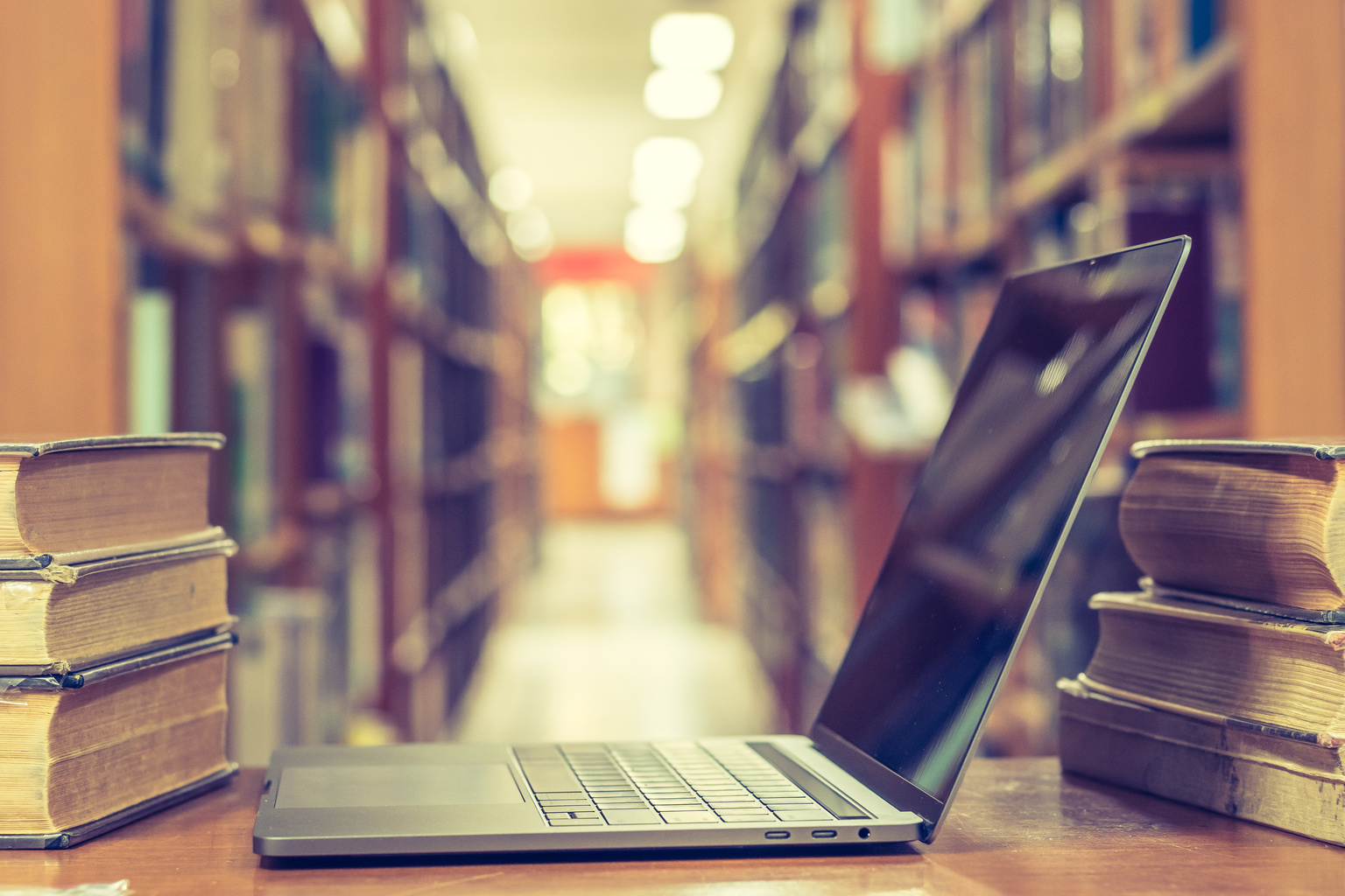 PC computer notebook open in blur school library among old stacks of book