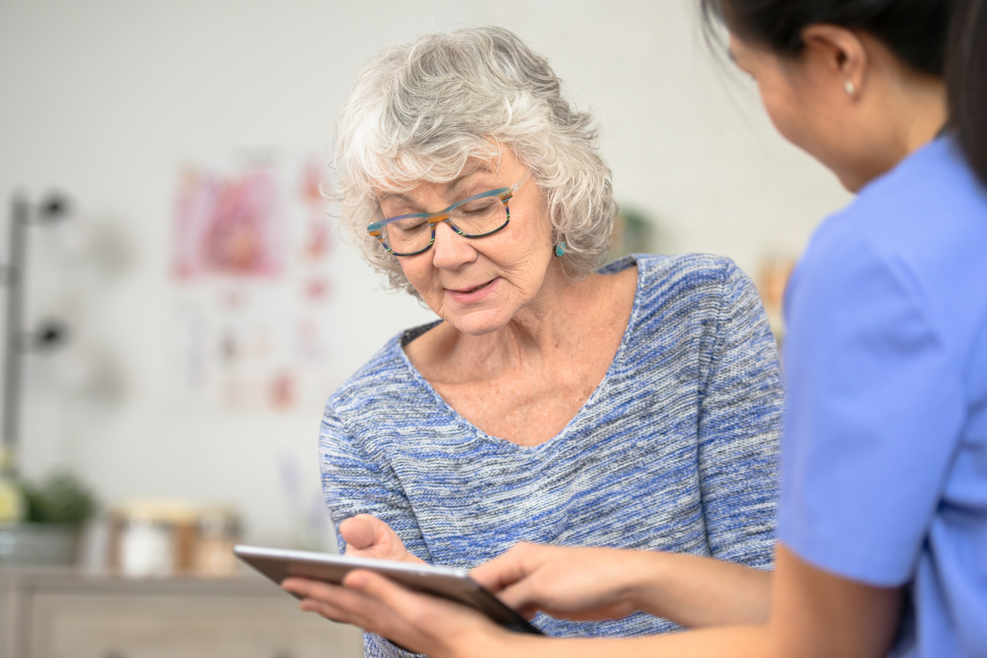 Senior patient reviews medical data on tablet with nurse