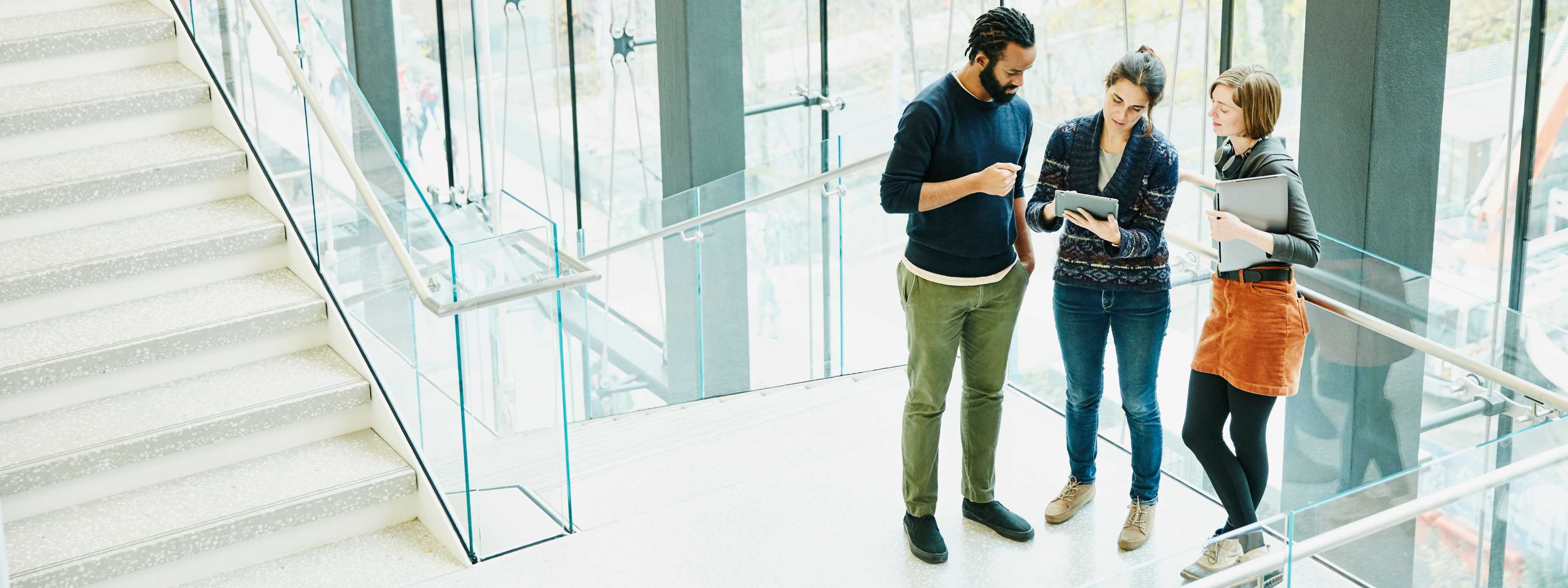 Man and two women reviewing tablet in office stairway