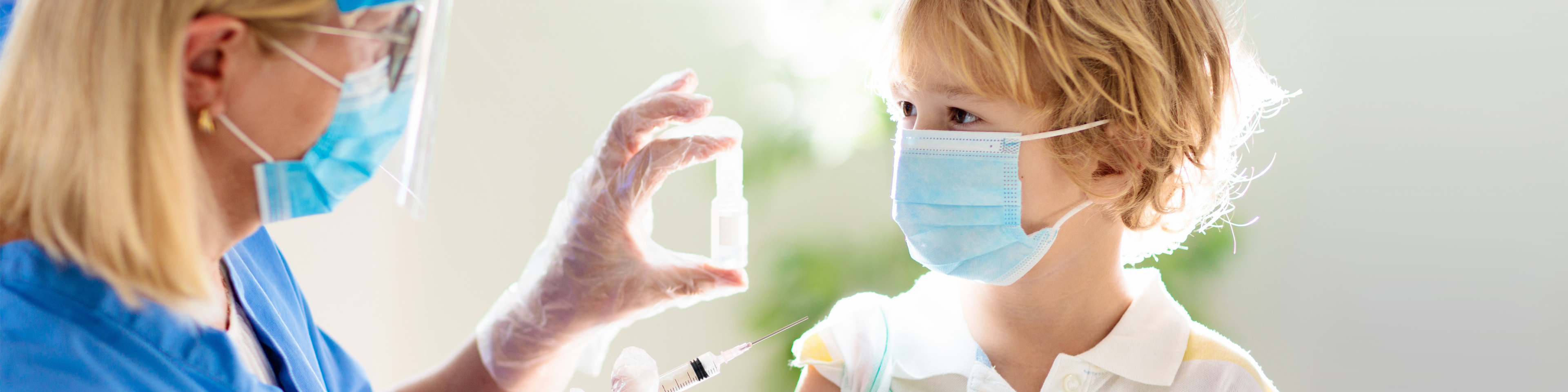 Mask and face shield wearing nurse getting ready to give mask wearing child a vaccination shot