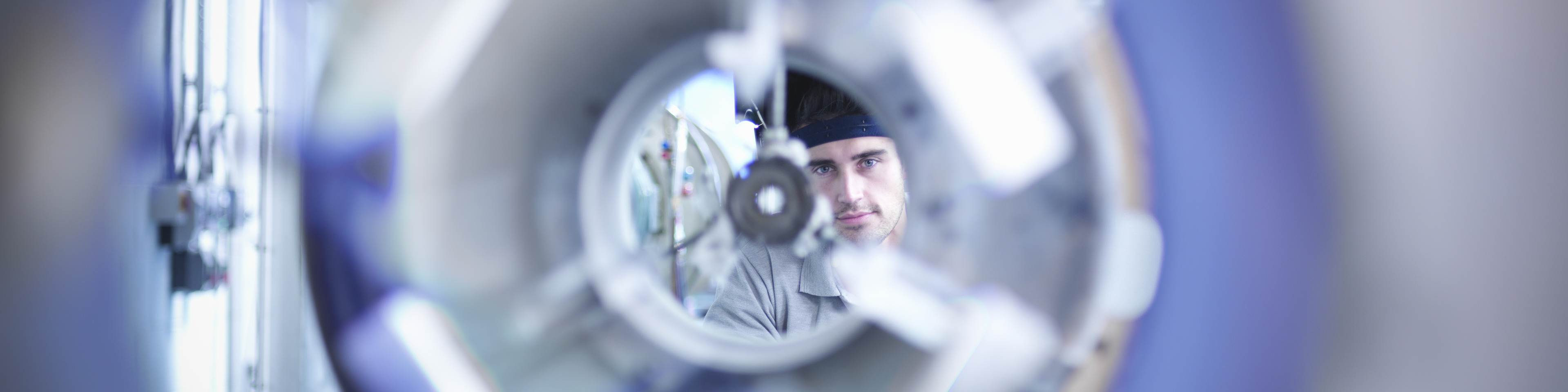 Industrial glass blower looking through glass forming lathe