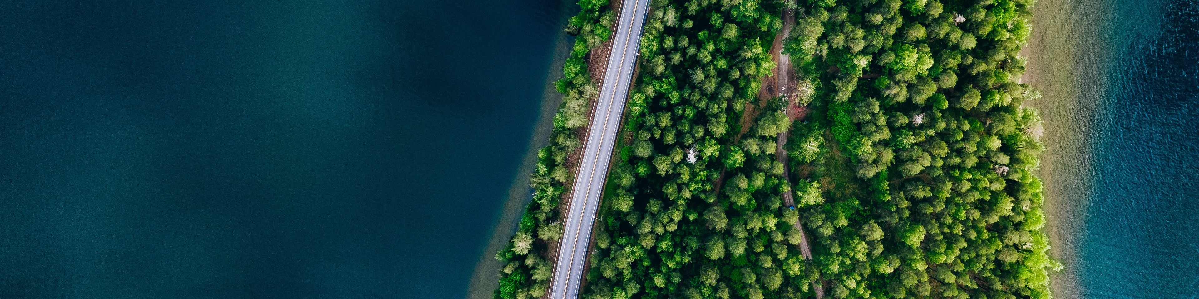 Aerial view of road between green forest and blue lake in Finland