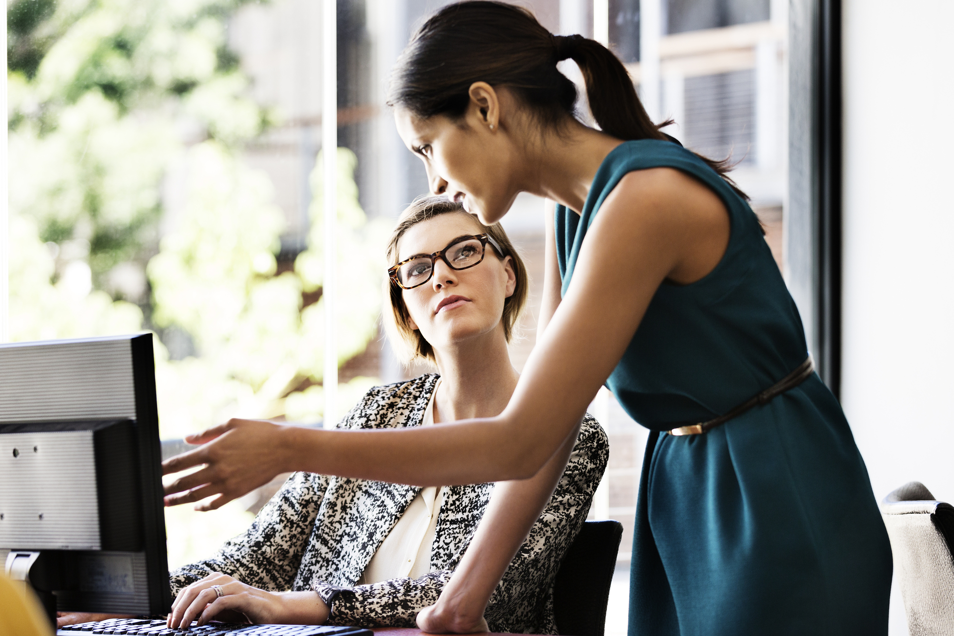 Businesswoman explaining something to female colleague over computer at desk in office