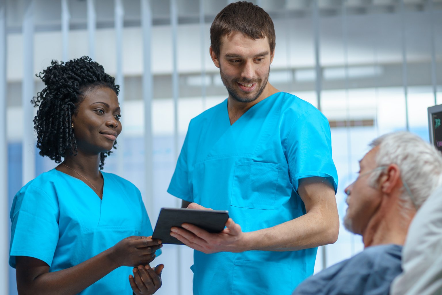 Two nurses consulting with patient in hospital bed