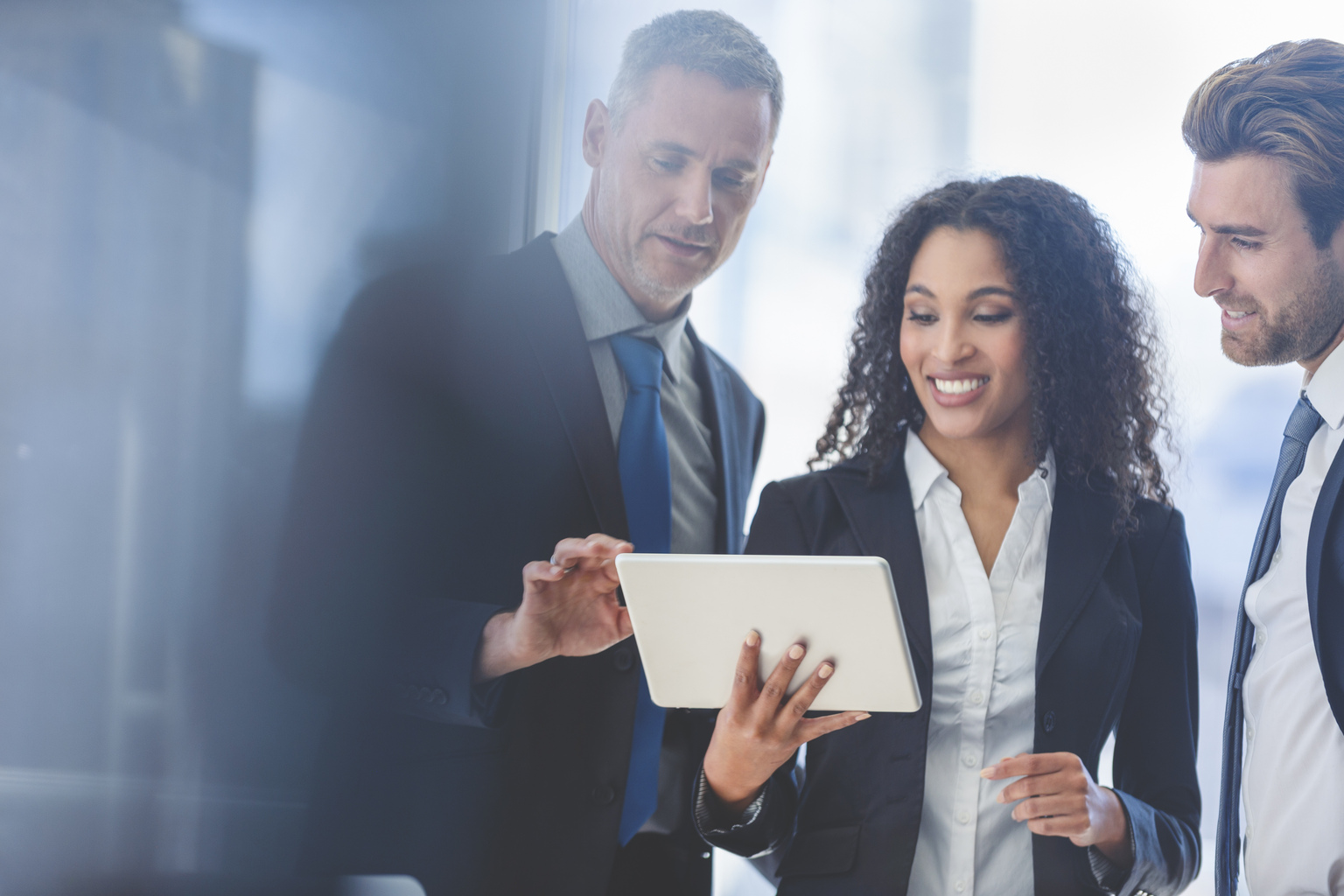 Business people meeting with a digital tablet. There is one businesswomen and two businessmen. They are all dressed in suits and having a discussion