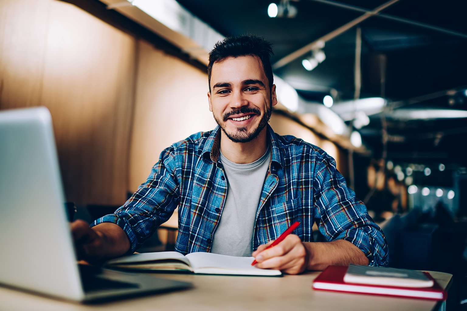 Cheerful male student learning in co-working office using laptop
