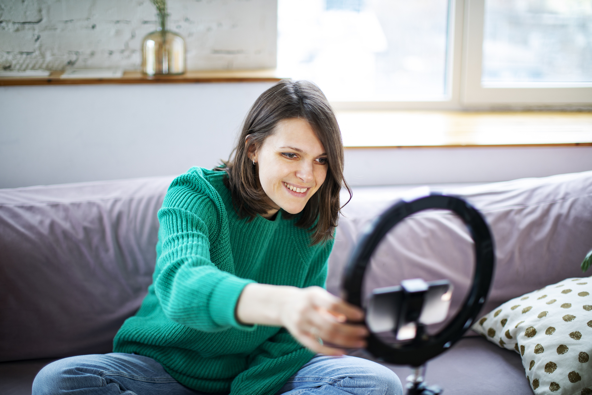 Young woman streaming live video with smartphone and ring light