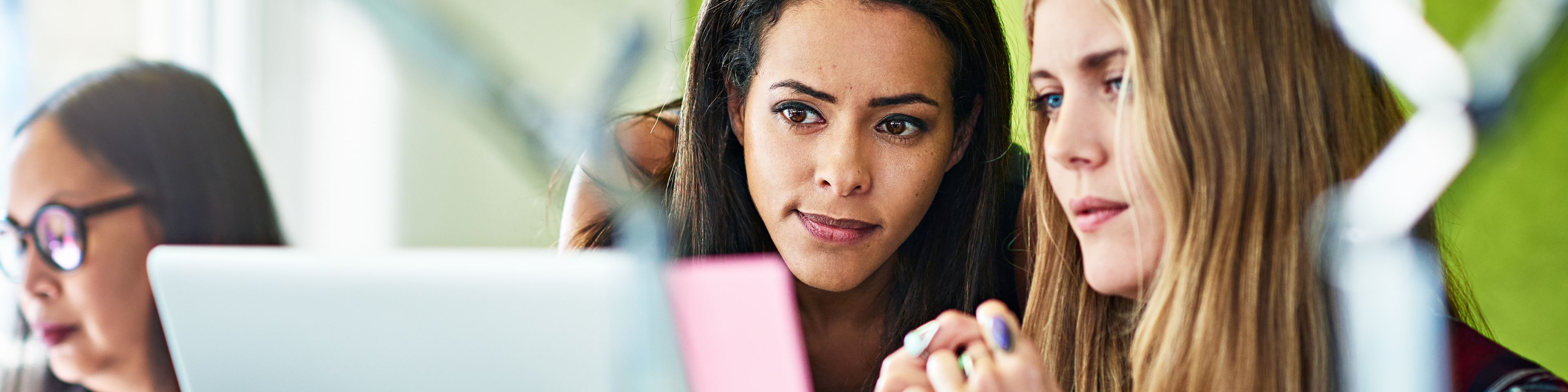 Two young businesswomen looking at laptop in office.