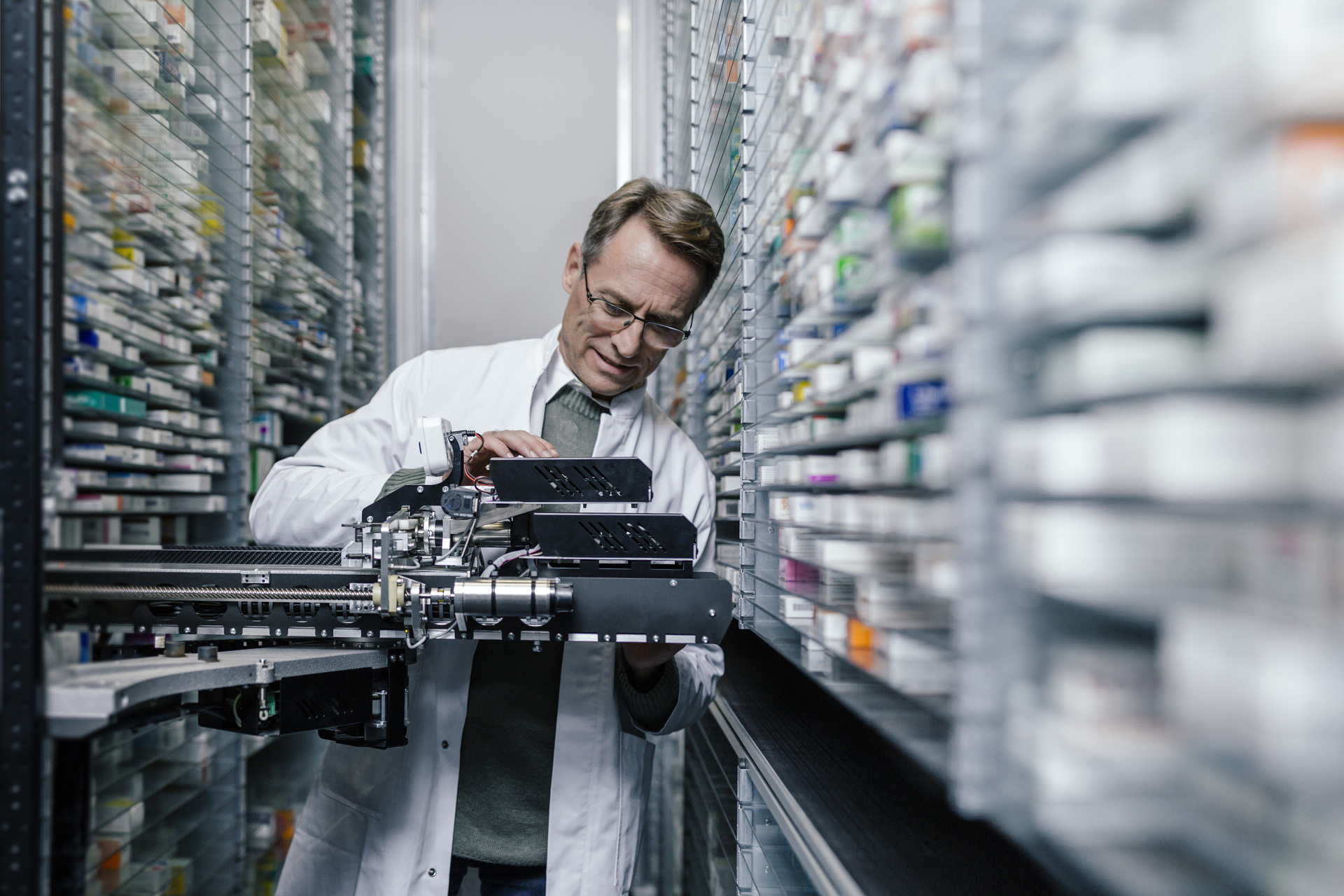 Mature white male pharmacist examining commissioning machine in pharmacy.