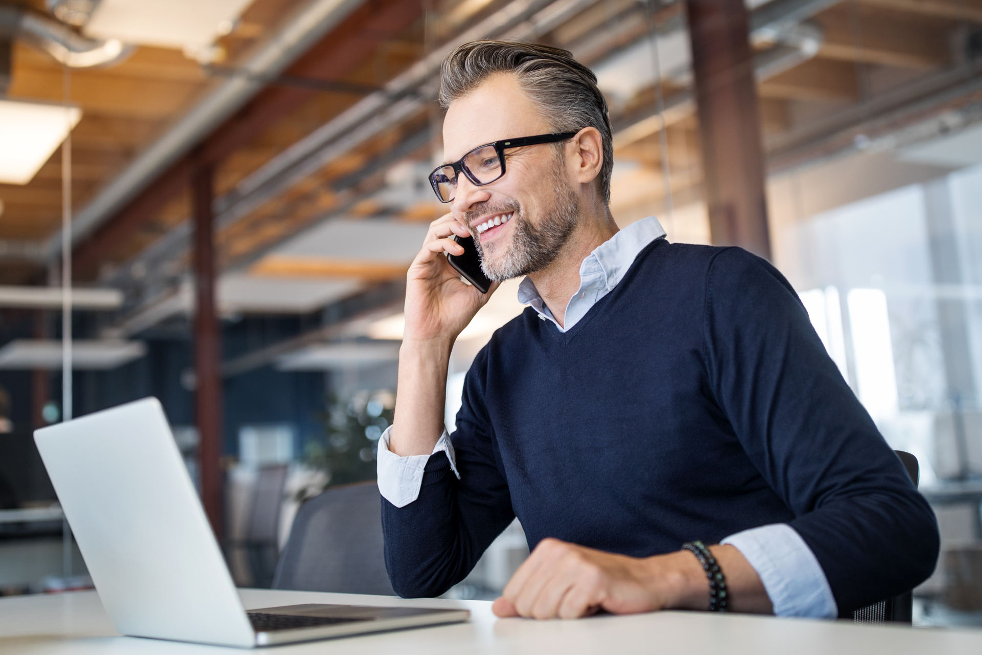 Mid adult business professional sitting at table with laptop and talking on mobile phone. Businessman working in office.