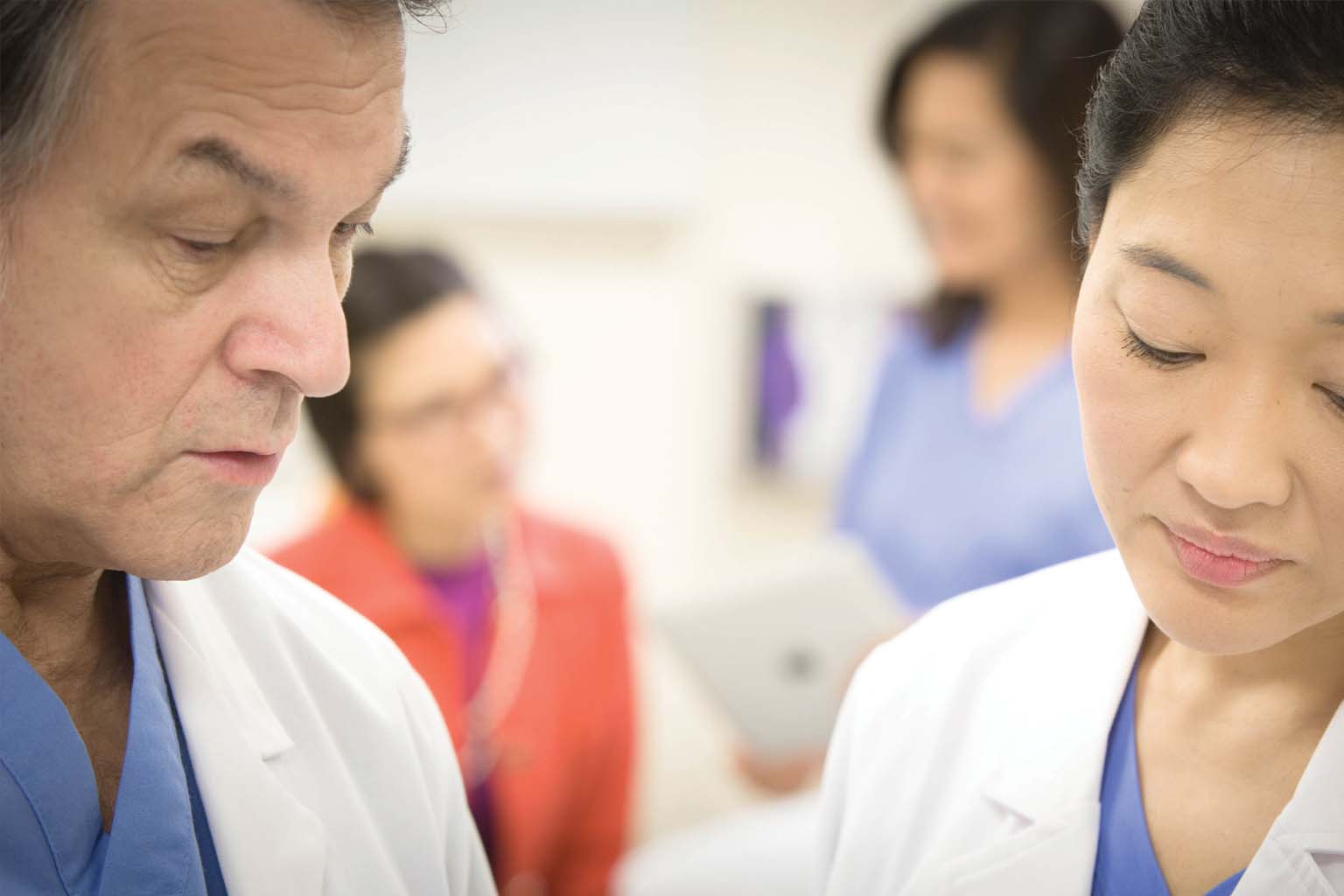 two doctors talking with patiient and nurse in background