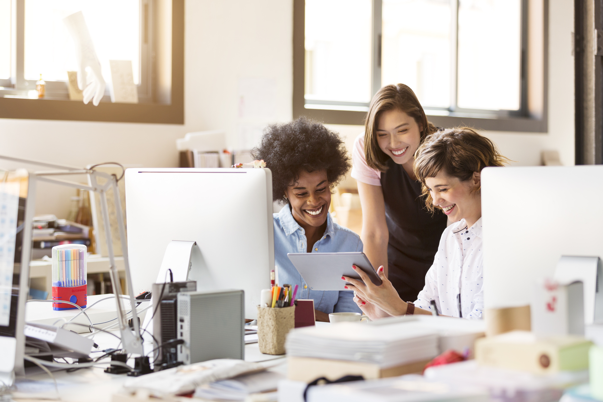 Happy multi-ethnic businesswomen using digital tablet at desk in office