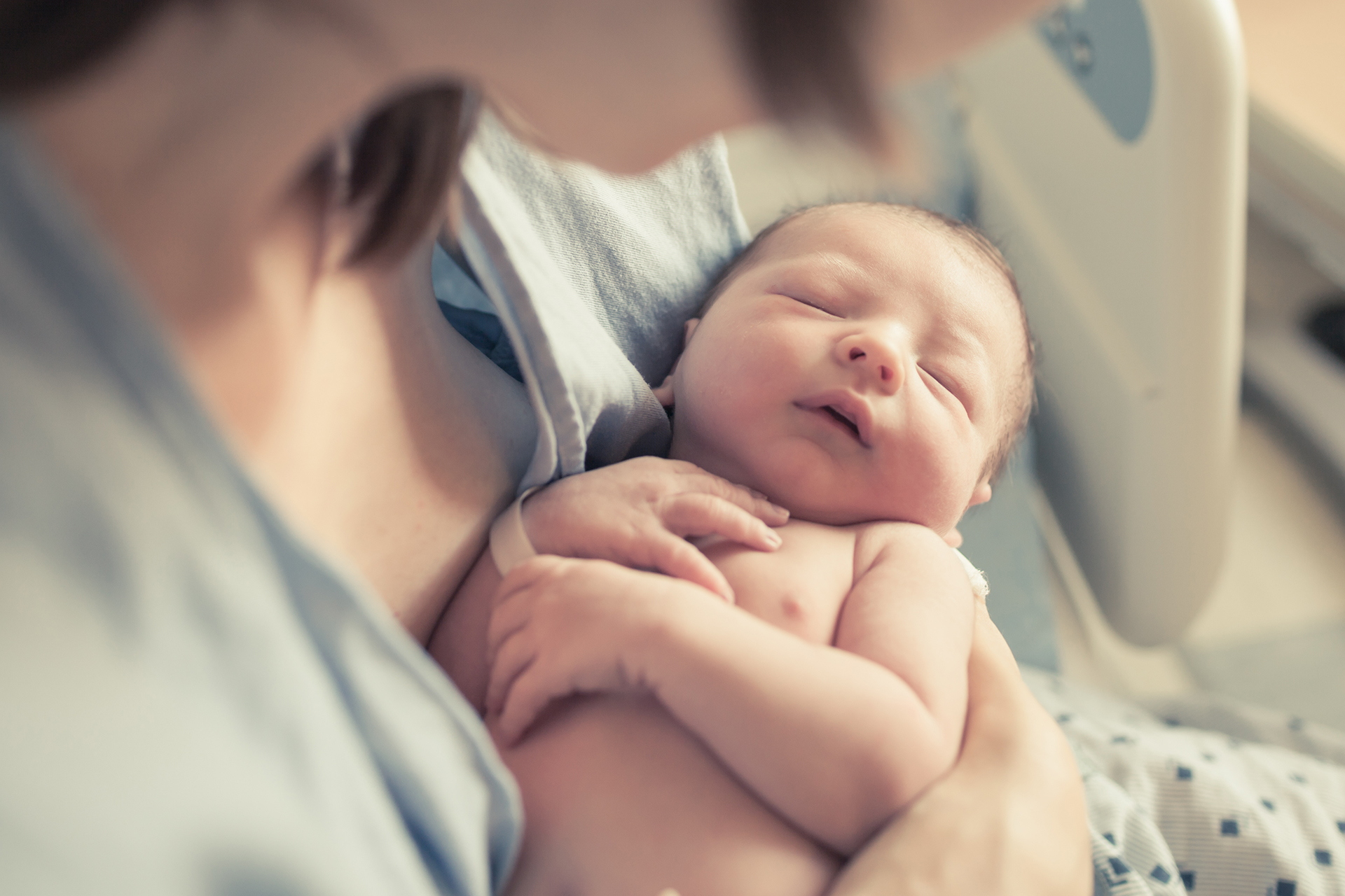 Close up on newborn cradled in mother's arm in hospital bed