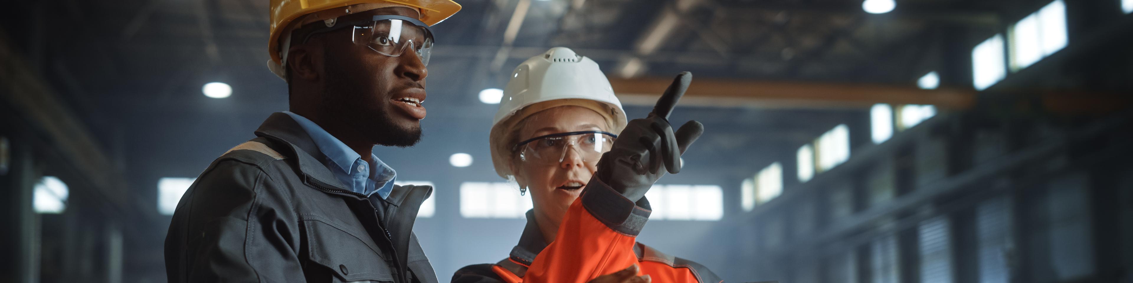 Two Heavy Industry Engineers Stand in Steel Metal Manufacturing Factory, Use Digital Tablet Computer and Have a Discussion. Black African American Industrial Specialist Talk to Female Technician.