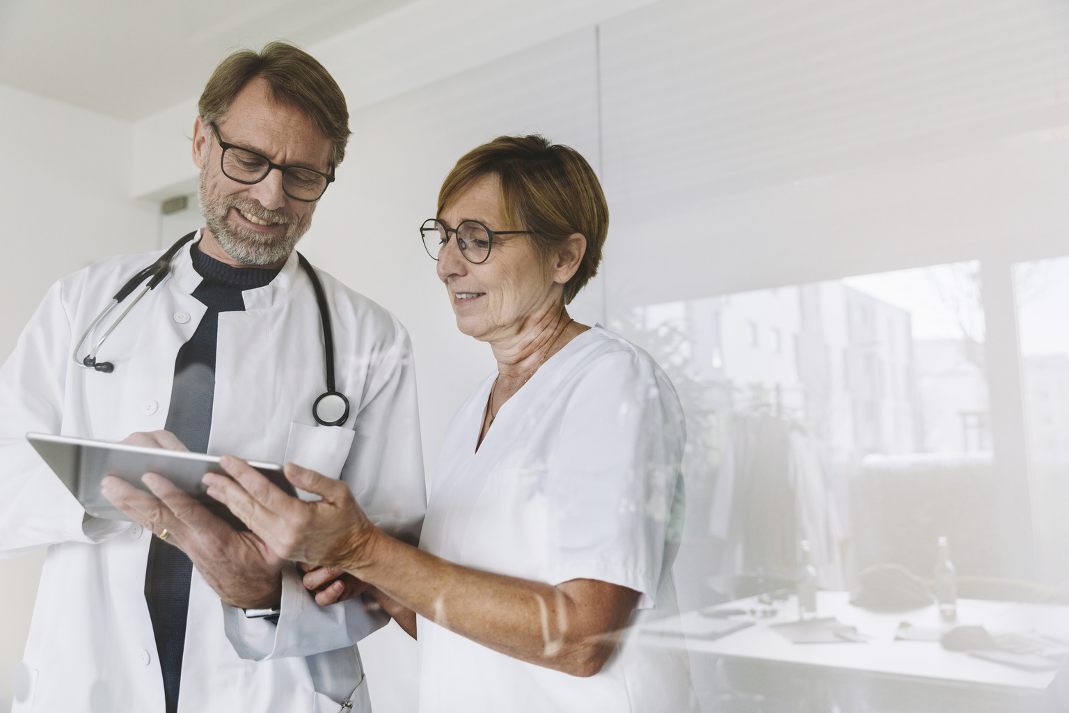 Doctor and assistant going over medical report or findings on digital tablet, Cologne, NRW, Germany