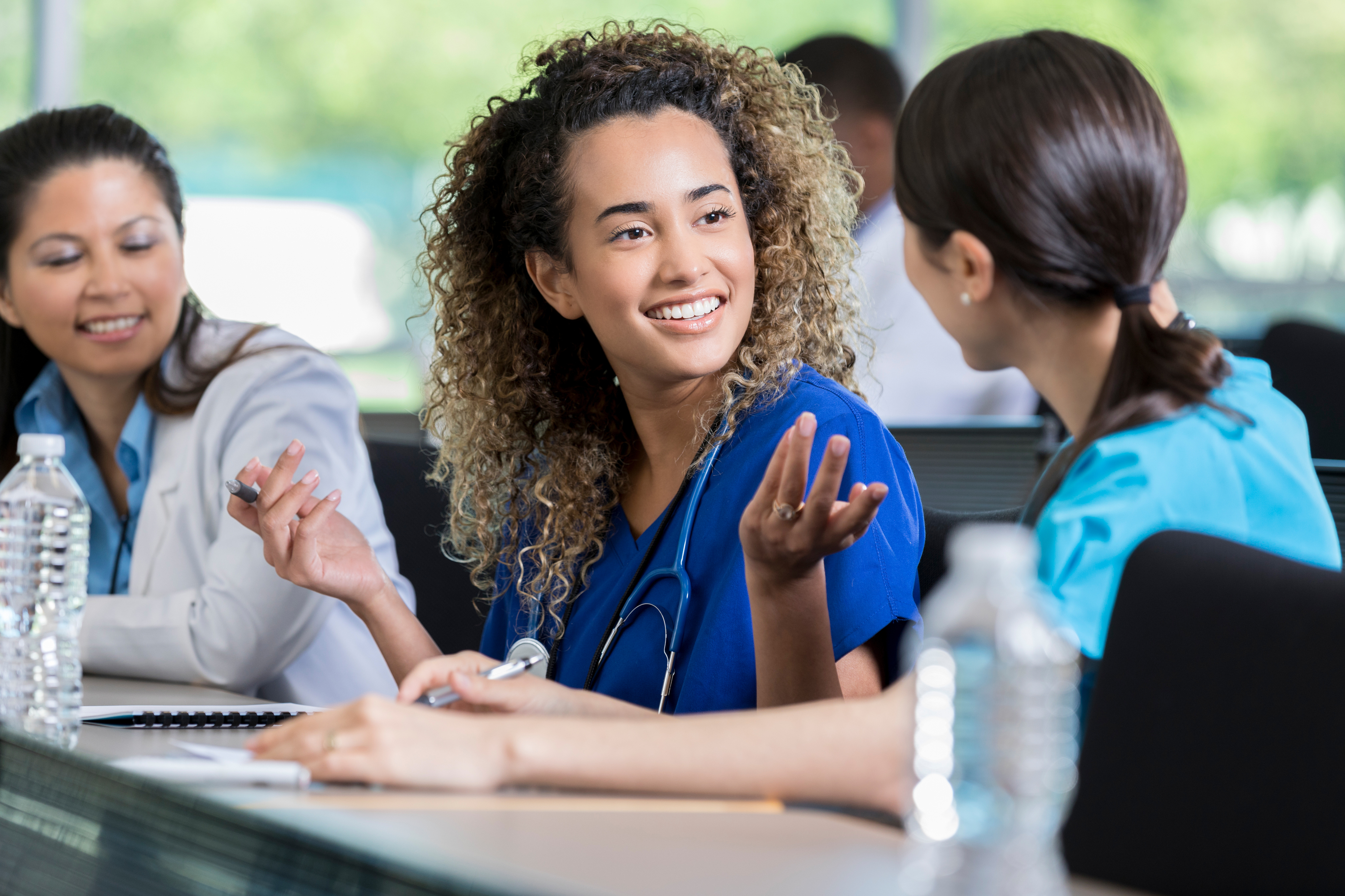 A nursing student wearing dark navy scrubs catches up with a classmate sitting next to her