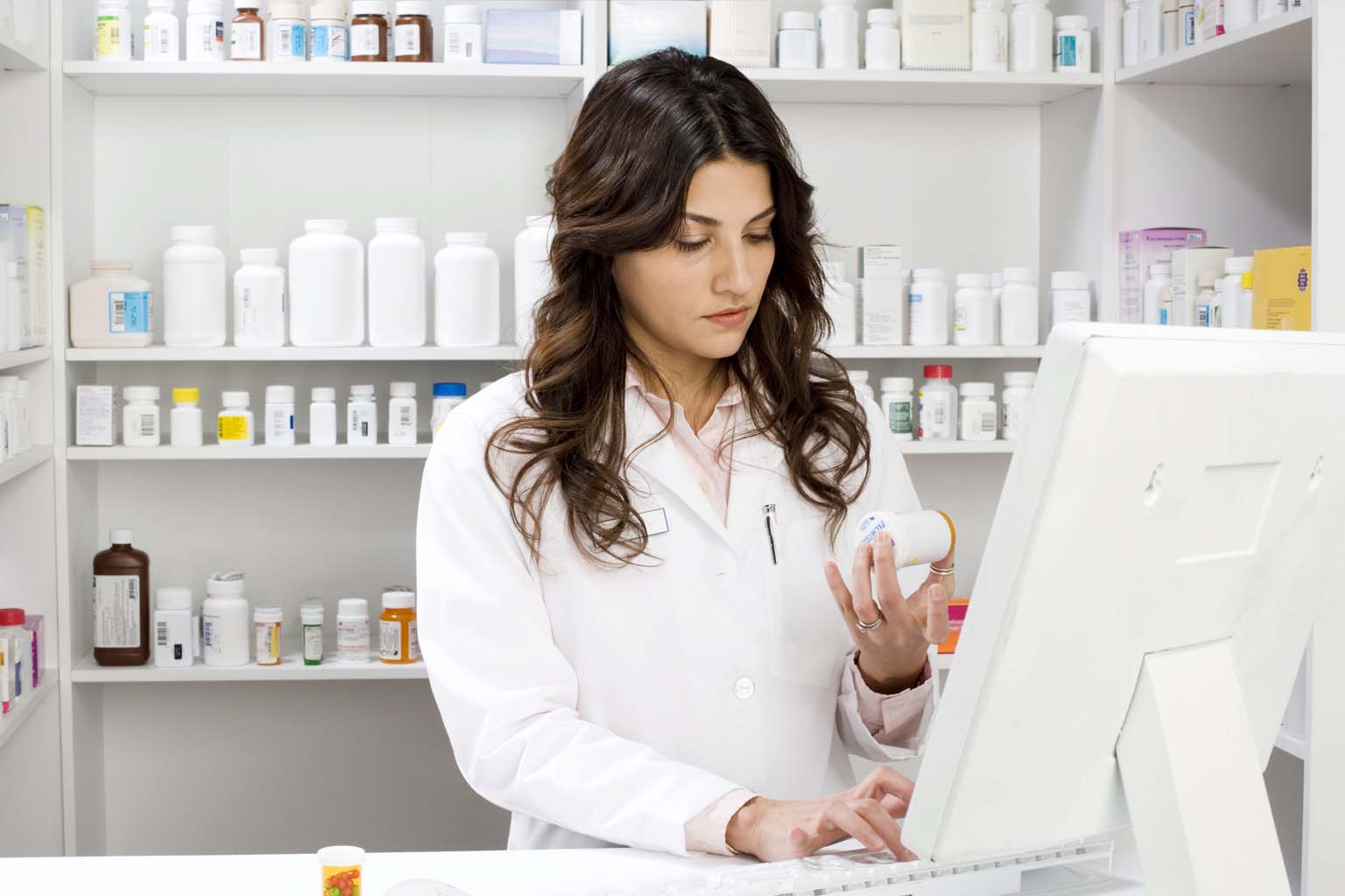 phamacist holding bottle of pills while using computer