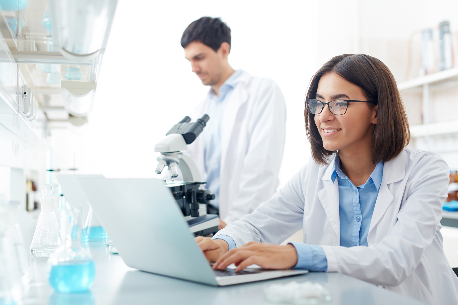 Medical professional conducting research in a lab using a laptop and microsope