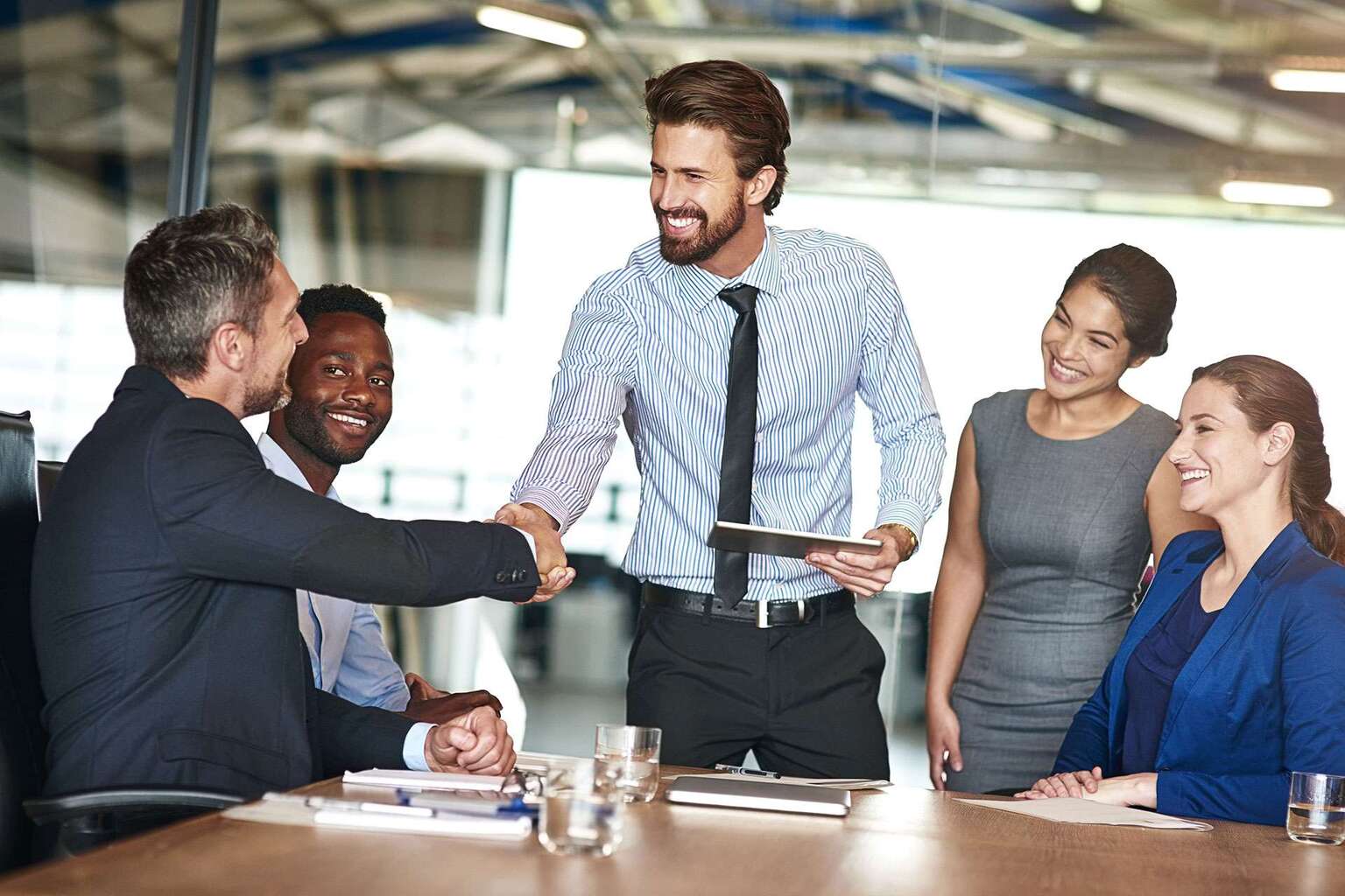 Professionals meeting and shaking hands while holding a tablet with TeamMate's audit management software.