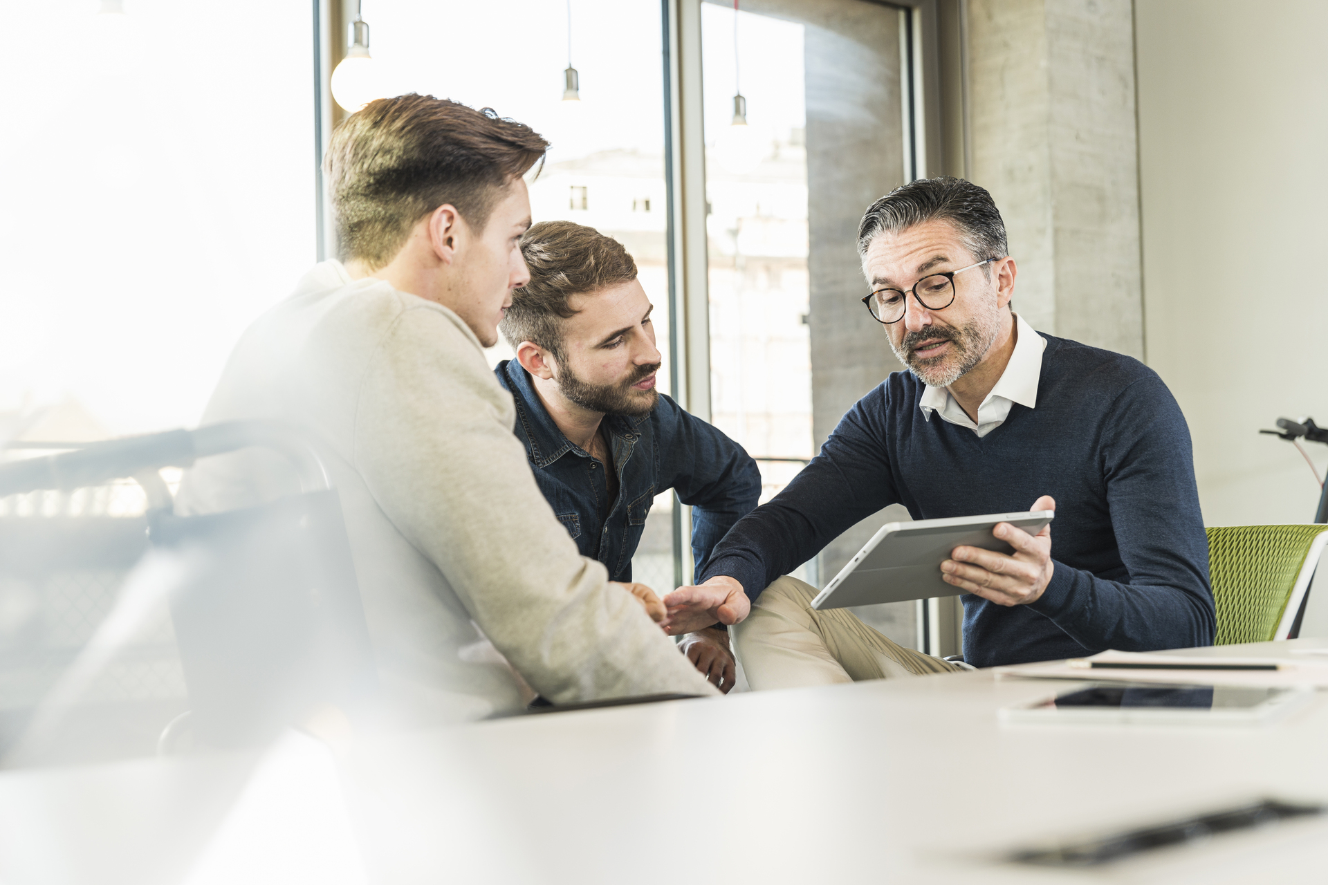 Three businessmen having a meeting in office sharing a tablet