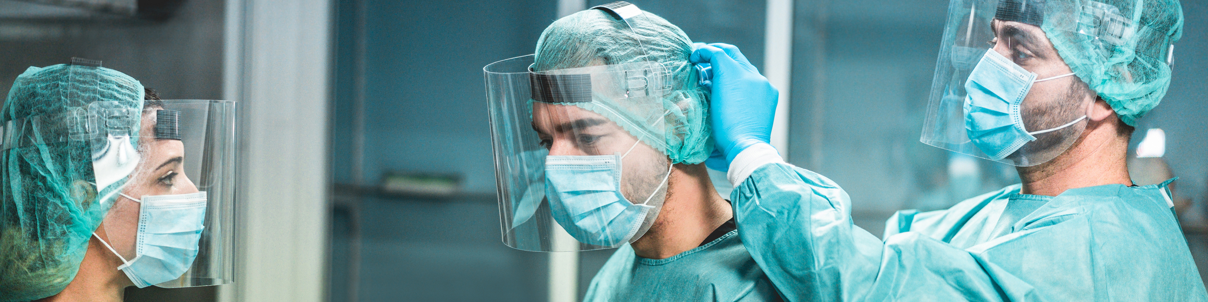 Three healthcare professionals getting in personal protective equipment