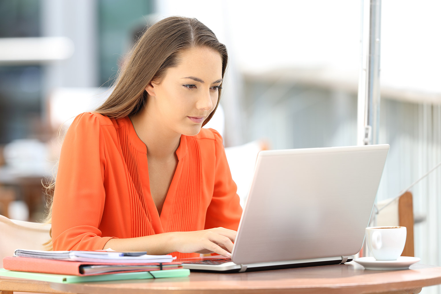 Studentka prawa w pomarańczowej bluzce pisze pracę dyplomową na laptopie korzystając z LEX Script