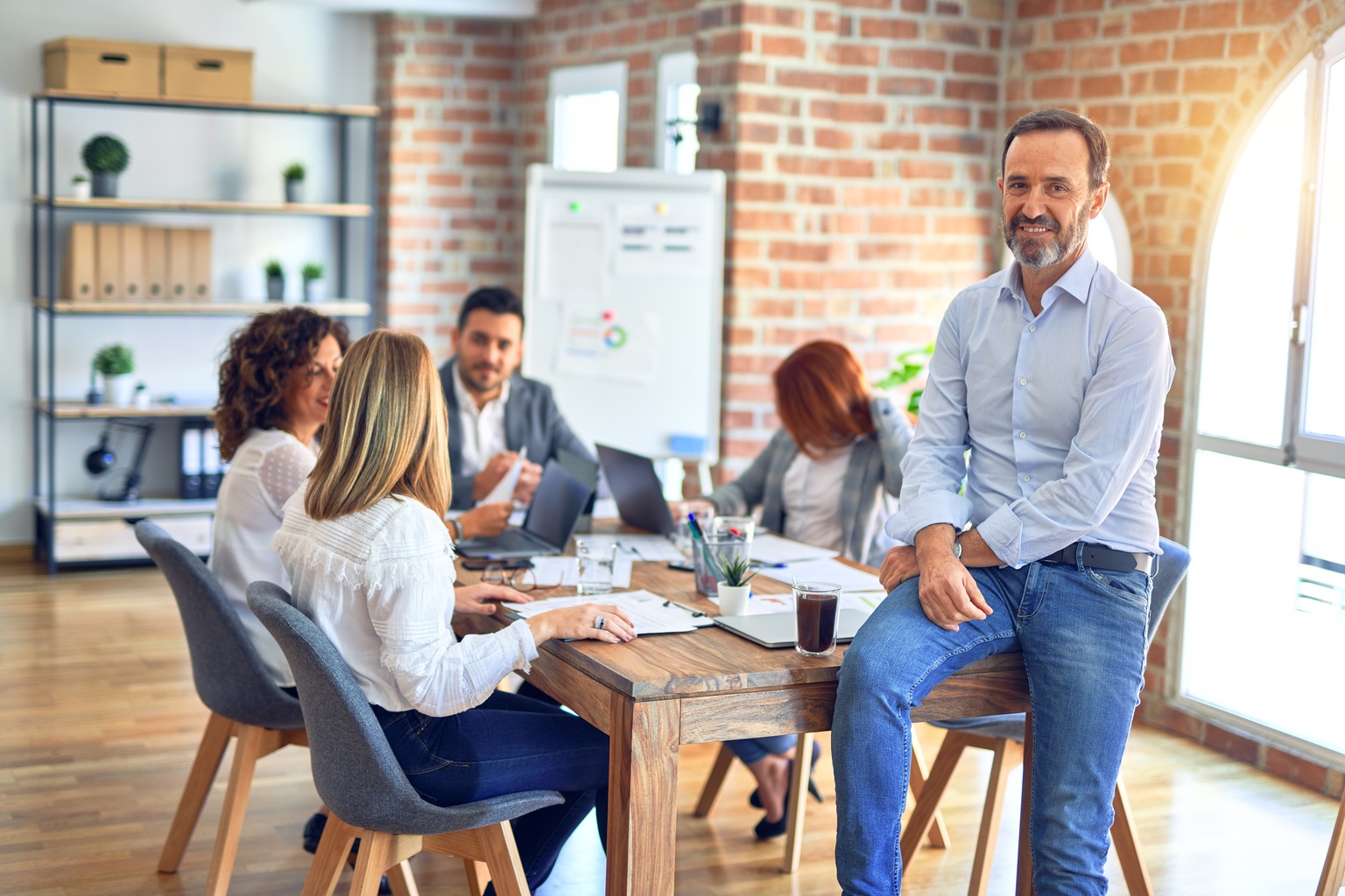 Group of business workers working together. Middle age handsome businessman standing smiling happy looking at the camera at the office