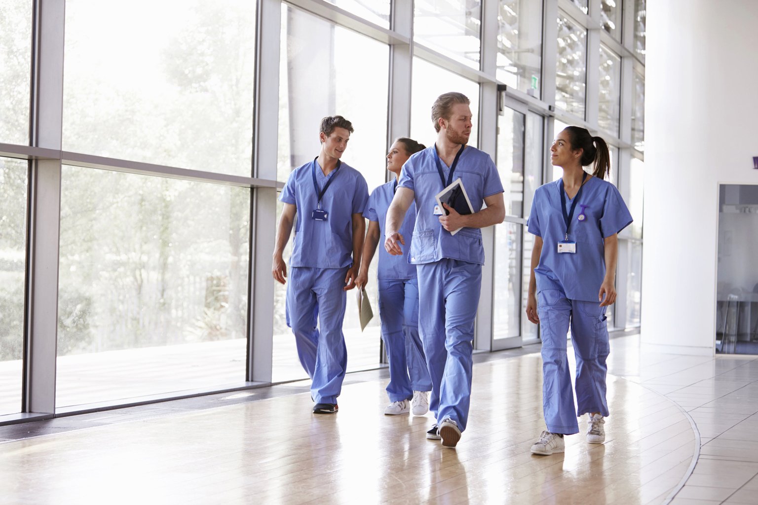 Four healthcare workers in scrubs walking in corridor